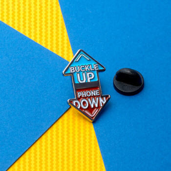Double-sided arrow lapel pin with 'Buckle Up' in blue and 'Phone Down' in red soft enamel.