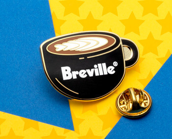 Breville brand lapel pin shaped like a black coffee cup with latte art on a blue and yellow star background.