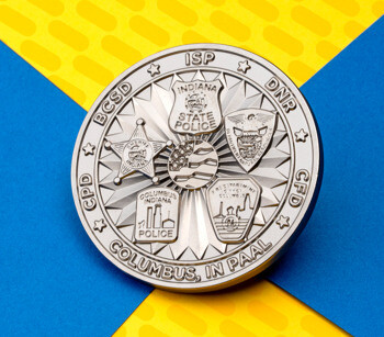 Silver challenge coin featuring Indiana State Police, BCSD, DNR, CFD, and CPD emblems with central flag design on a blue and yellow background.