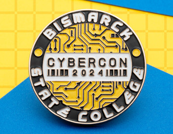 Circular Bismarck State College Cybercon 2024 lapel pin featuring a yellow circuit board design with black and white enamel text.