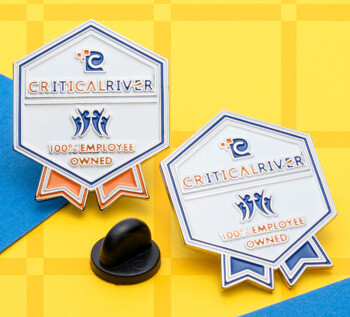 Hexagonal CriticalRiver lapel pins with ribbon base featuring the text 100% Employee Owned and a blue and orange color scheme.