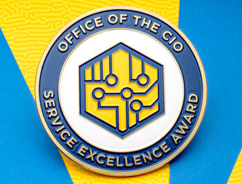 A circular challenge coin for the Office of the CIO Service Excellence Award, featuring a blue border and yellow circuit board icon in a hexagon.