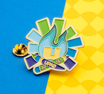 Soft enamel lapel pin featuring a stylized flame, paintbrush, and the text UPAD 2025 in blue, green, and purple.