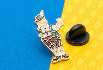 Enamel lapel pin featuring a man in traditional Bavarian lederhosen holding a beer mug, shown with a black rubber clutch.