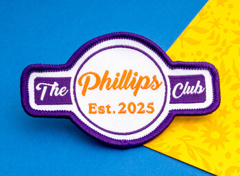 Embroidered patch for The Phillips Club Est. 2025 featuring purple borders and orange lettering on a white background.