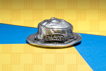 Antiqued silver bucket hat medallion with TITANS text on the front band, resting on a yellow and blue background.